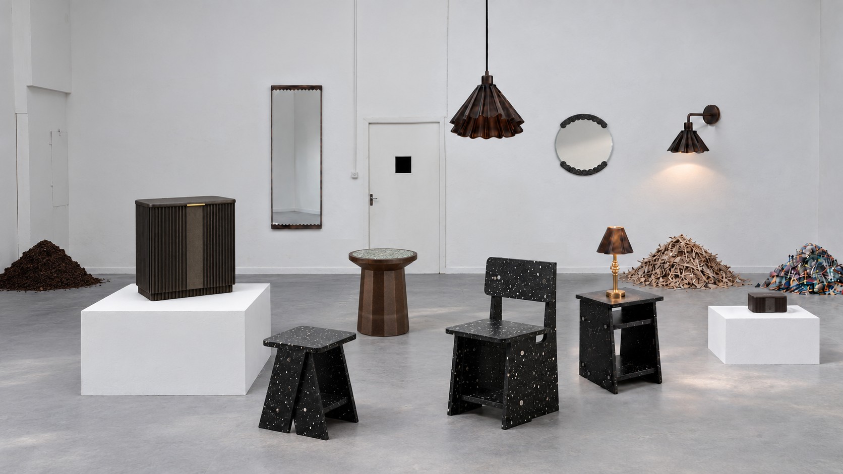 MadeBy recovered-material chair, stool, table and lighting arranged in a studio with piles of the coffee, wood and plastic waste they came from
